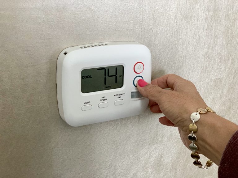 Woman setting the thermostat to keep the home at confortable temperature during seasons